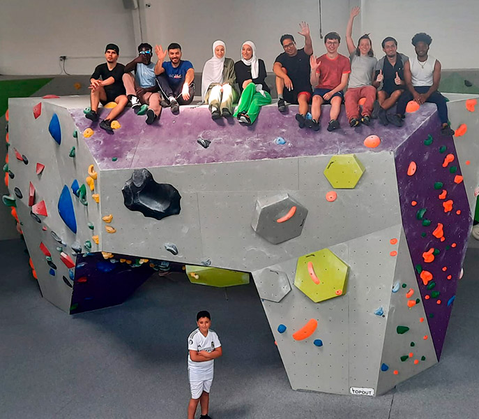 Junge PoC sitzen stolz auf einem hohen Boulderklotz und winken